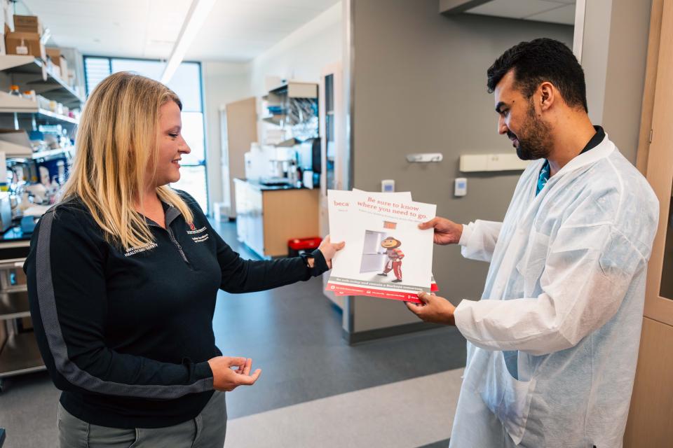 Jenna Dickerson is seen giving a student researcher a poster that says, "Be safe today remain a Buckeye tomorrow"